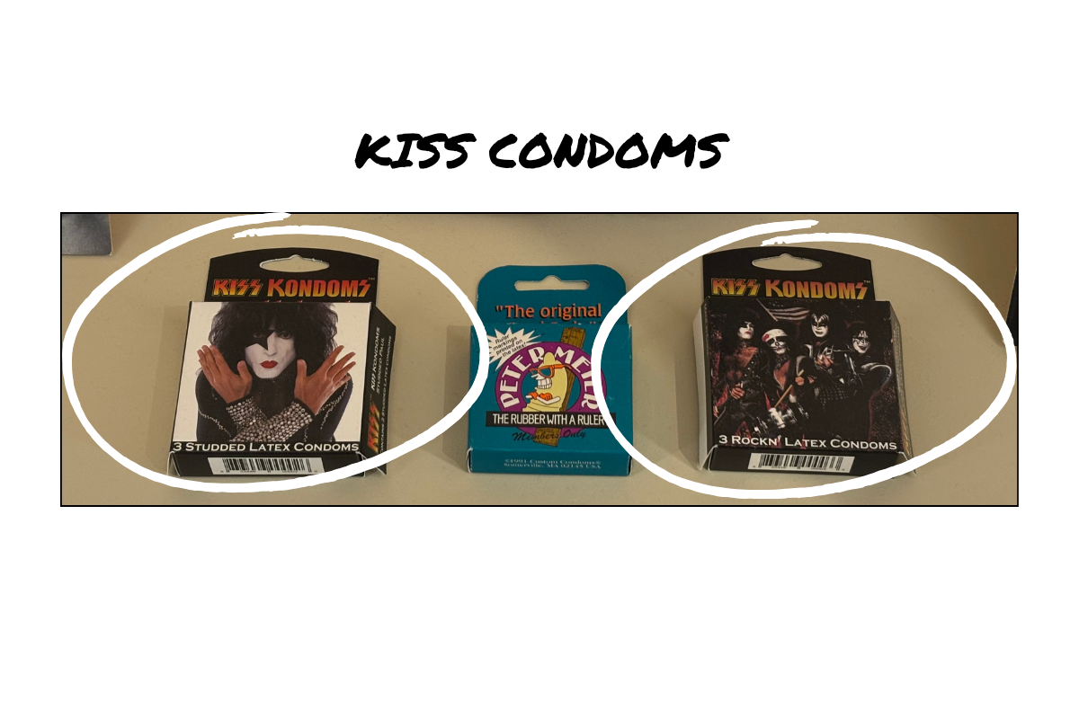 The image shows Kiss Condoms packaging in a display case at the Museum of Sex Miami. The image shows two versions of the Kiss Kondoms packaging. Both packaging variations are black and white with images of Kiss. The Peter Meter is in between the two Kiss Kondom packages in the display case.